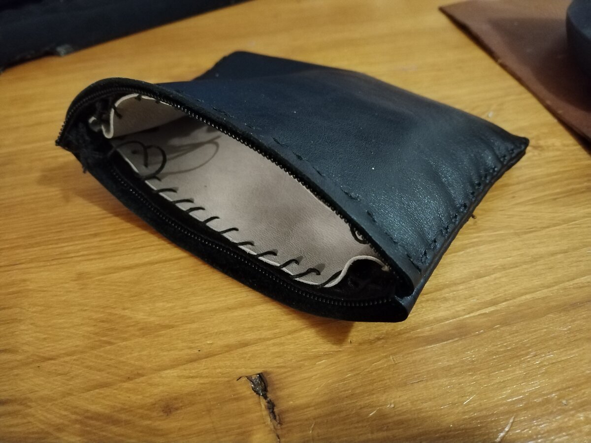 Pochette en cuir noir teint à l'huile, ouverte sur une doublure beige, couture sellier blanche