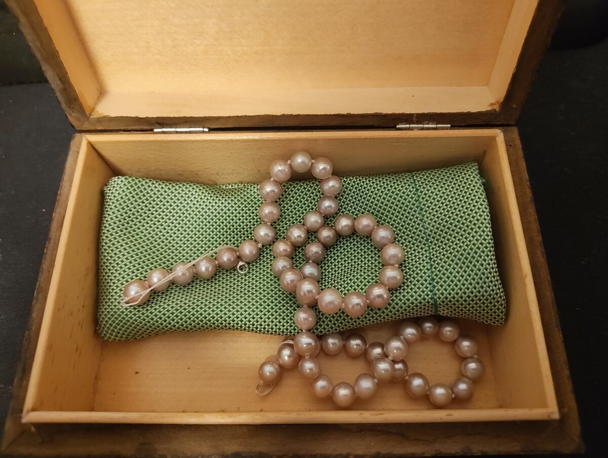 Collier de perles posé sur un coussin de soie verte dans une boîte en bois